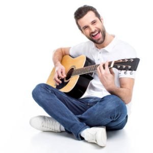 Smiling young man sitting and playing guitar on white
